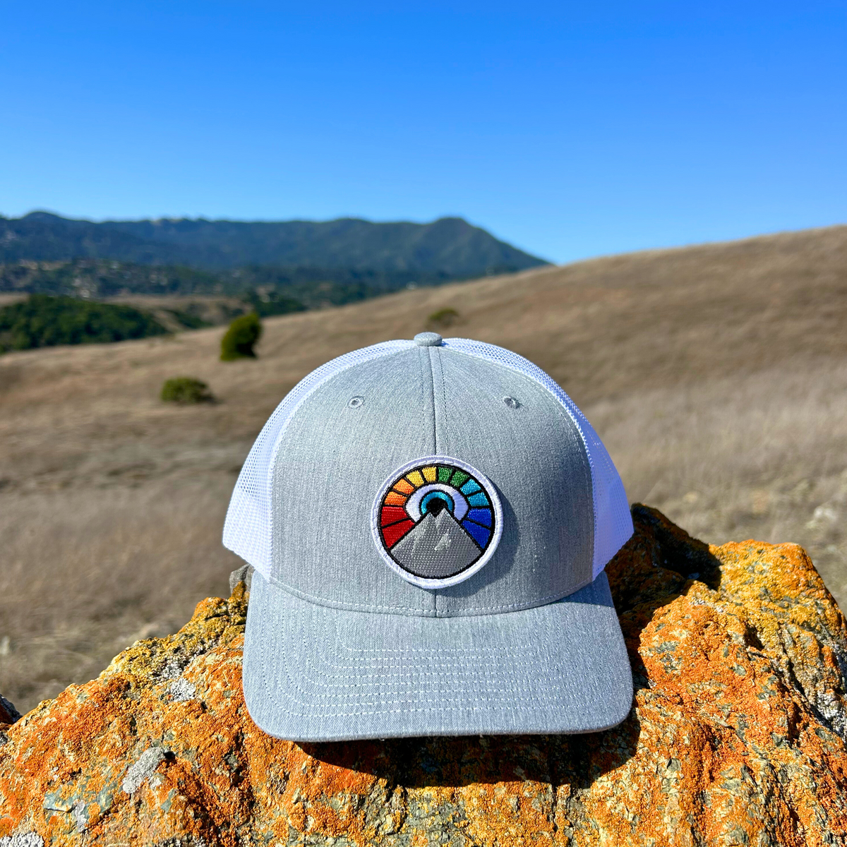 Light gray and white Kooh Culture trucker hat with the Evil Eye Sun patch in Rainbow Edition colours