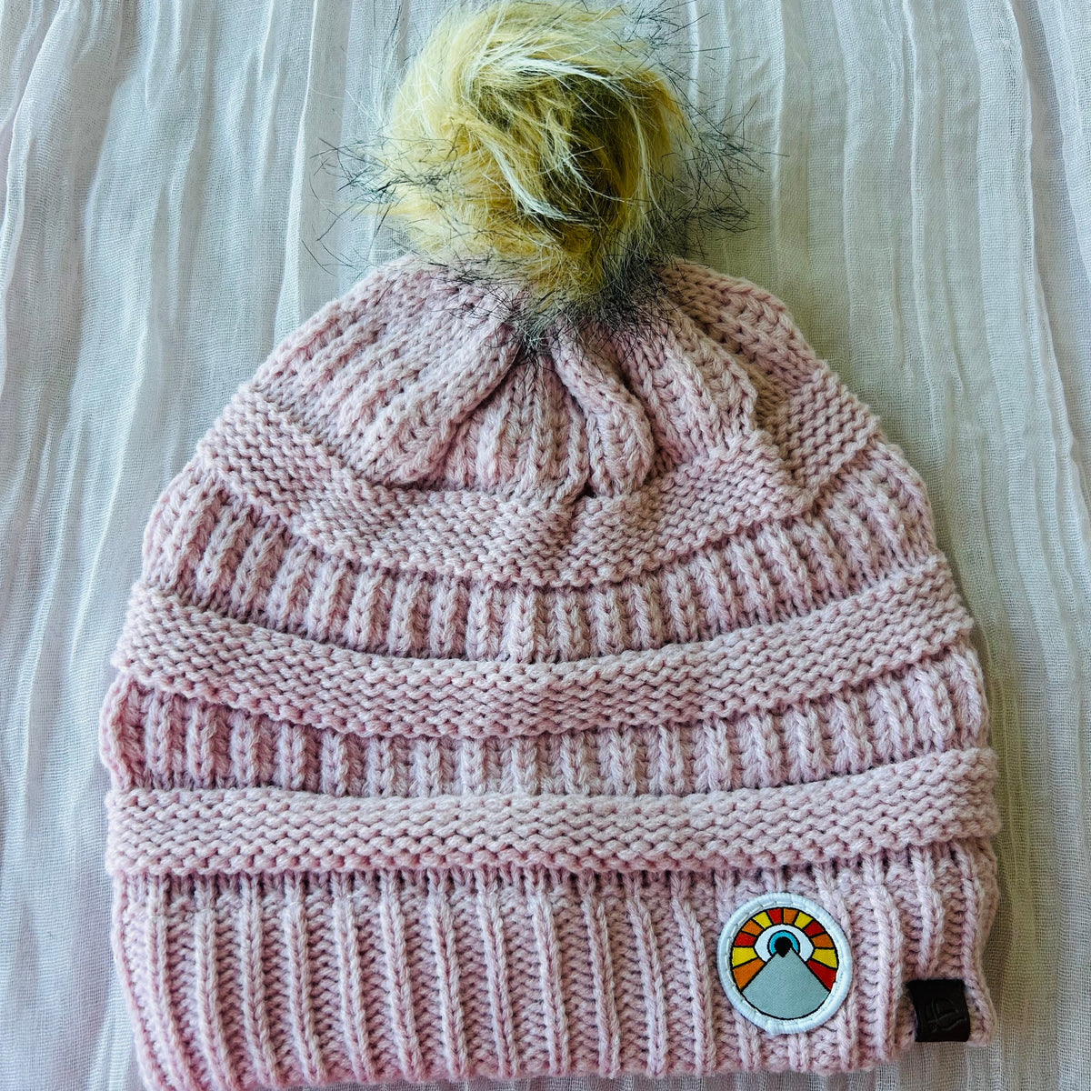 Light pink Kooh Culture pom beanie with the Mini Evil Eye Sun patch