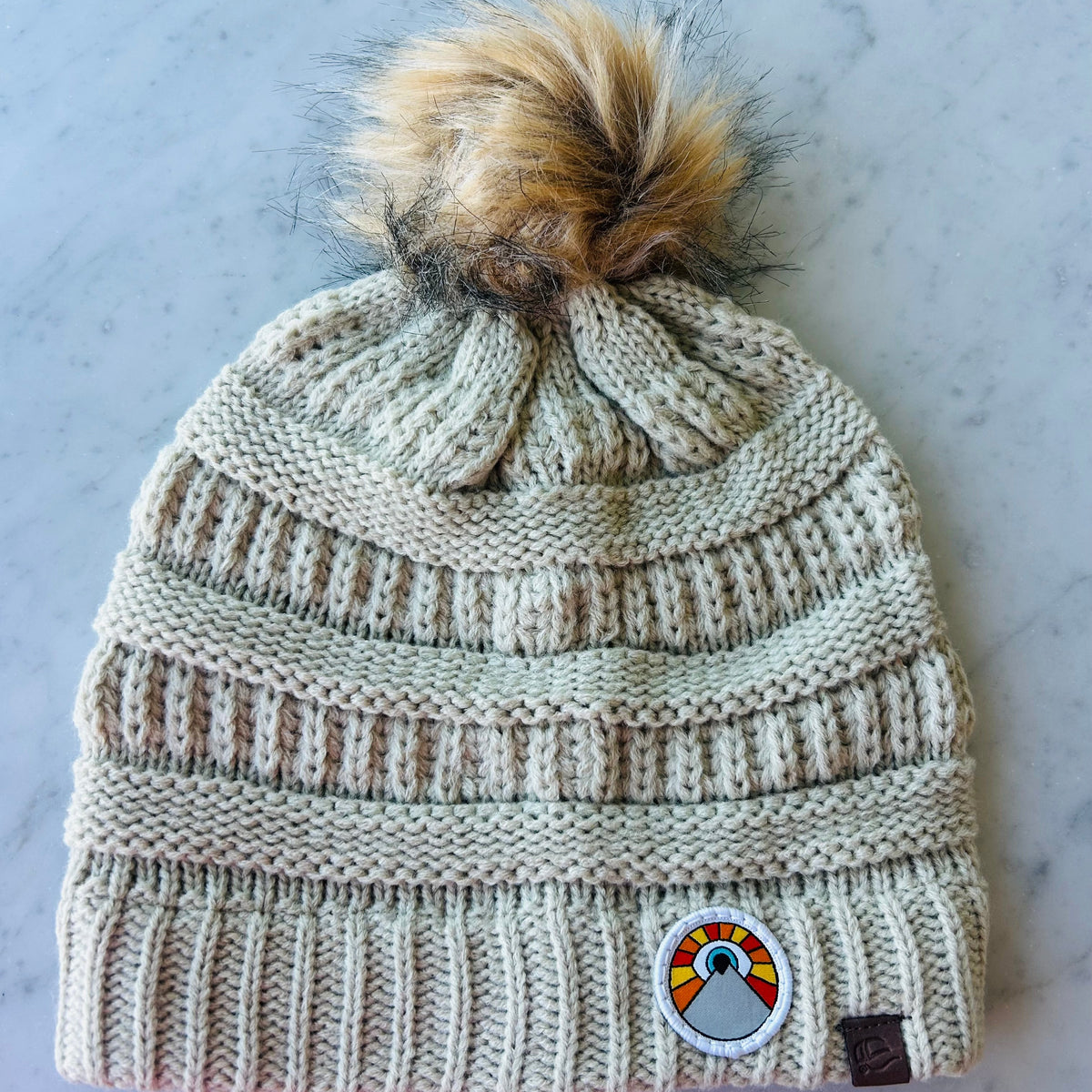 Beige Kooh Culture pom beanie with the Mini Evil Eye Sun patch