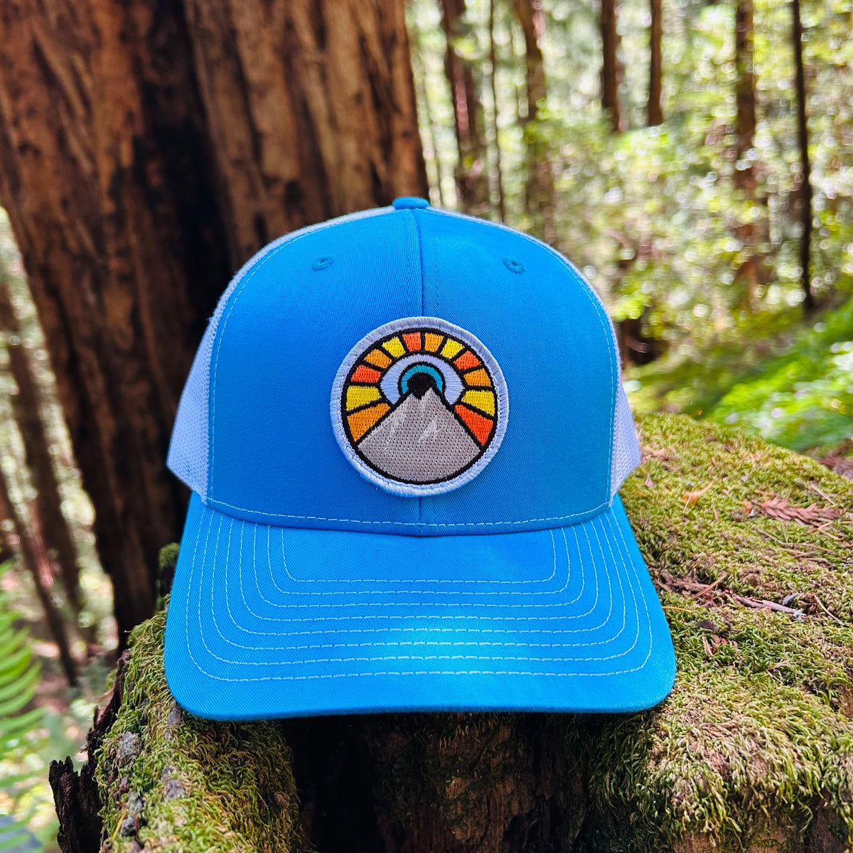 Cyan blue and white Kooh Culture trucker hat with the Evil Eye Sun patch