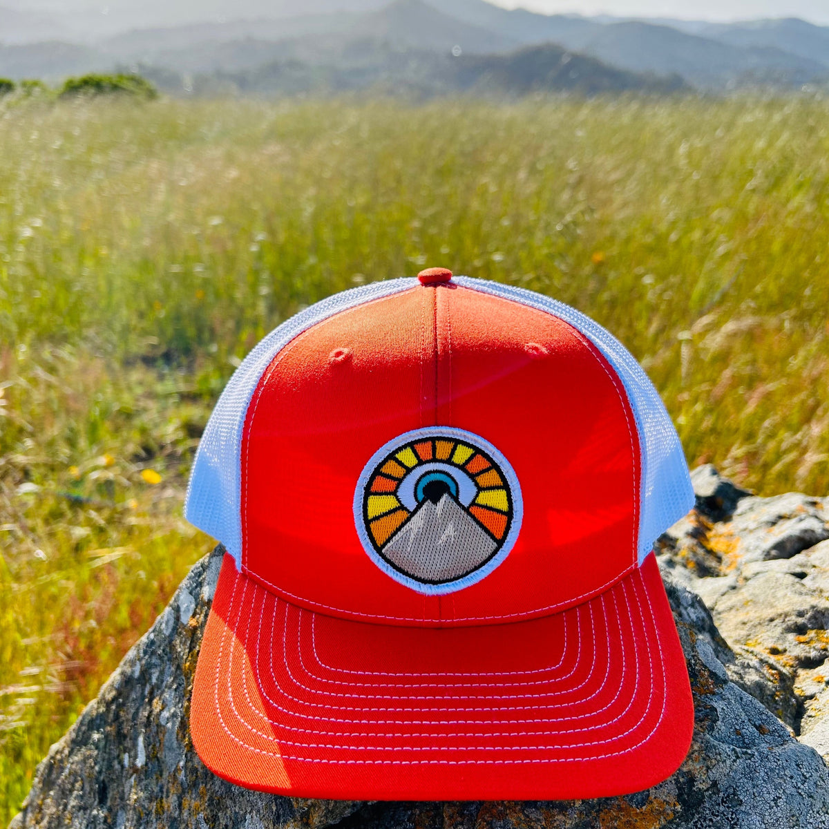 Orange and white Kooh Culture trucker hat with the Evil Eye Sun patch