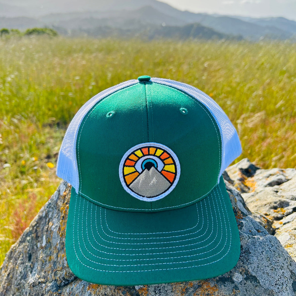 Kelly green and white Kooh Culture trucker hat with the Evil Eye Sun patch