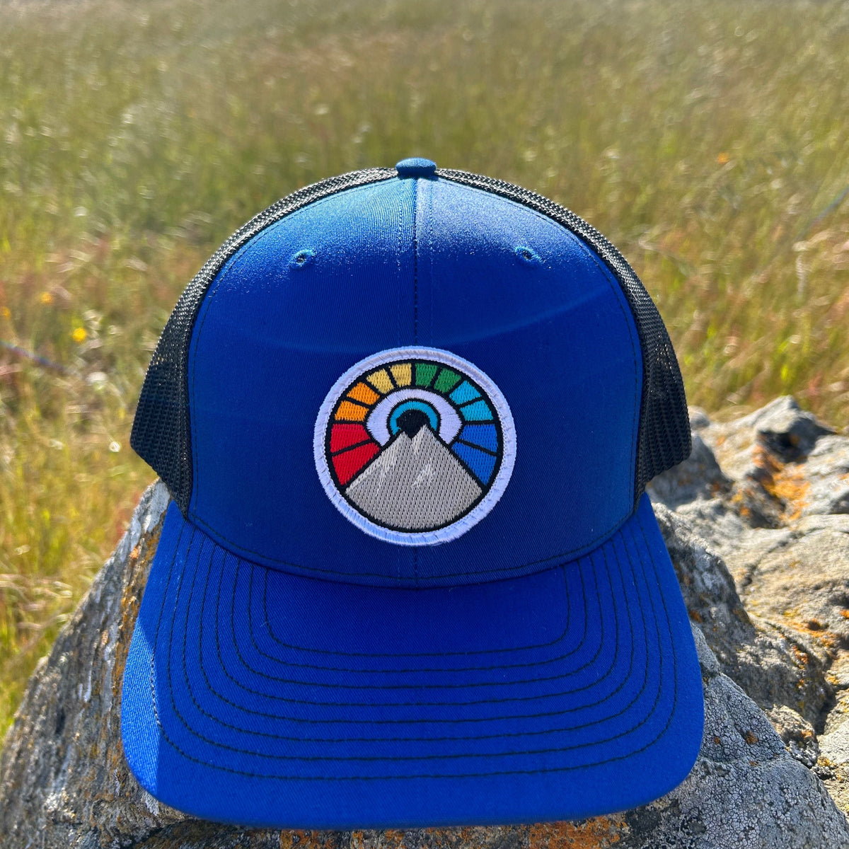Royal blue and black Kooh Culture trucker hat with the Evil Eye Sun patch in Rainbow Edition colours