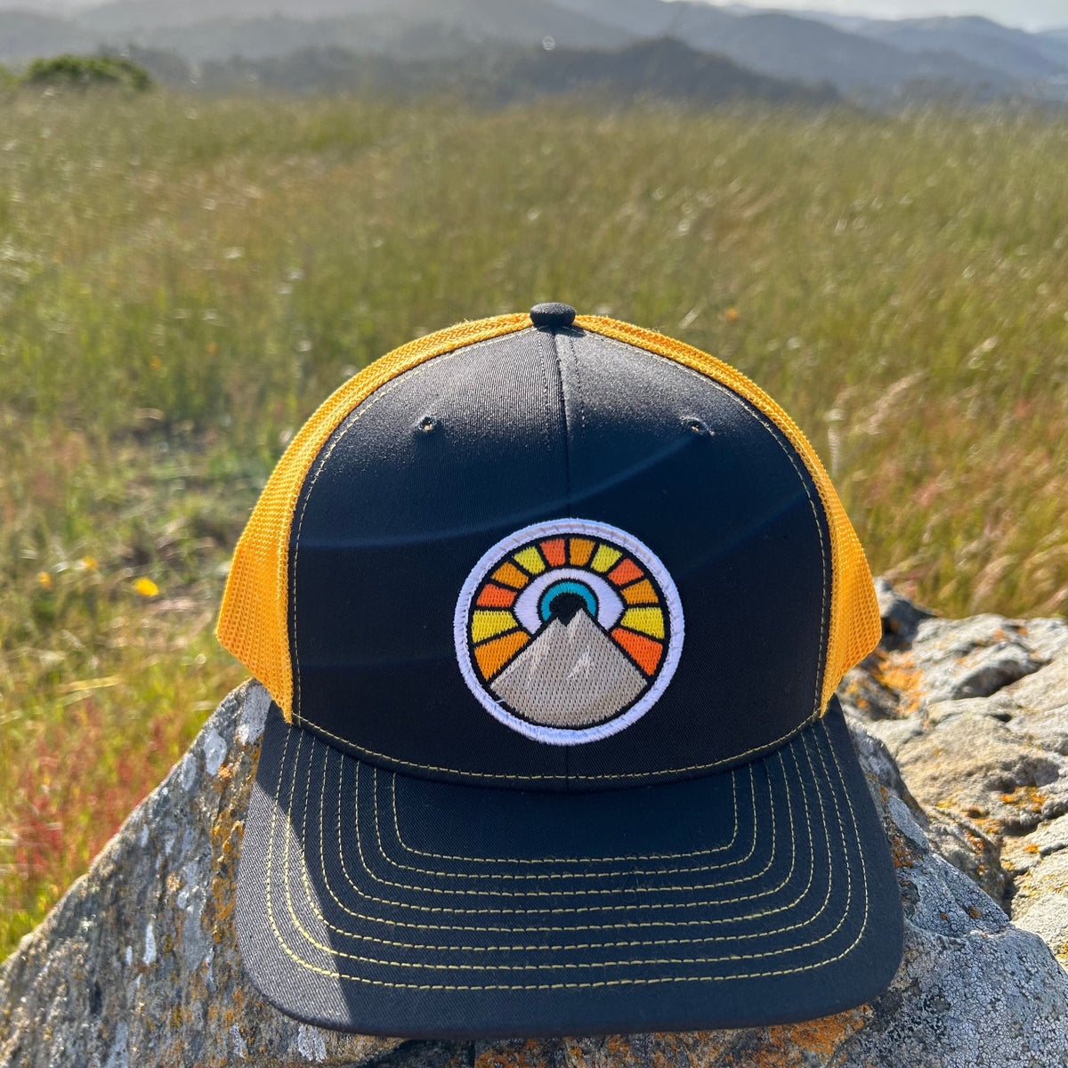 Black and gold Kooh Culture trucker hat with the Evil Eye Sun patch