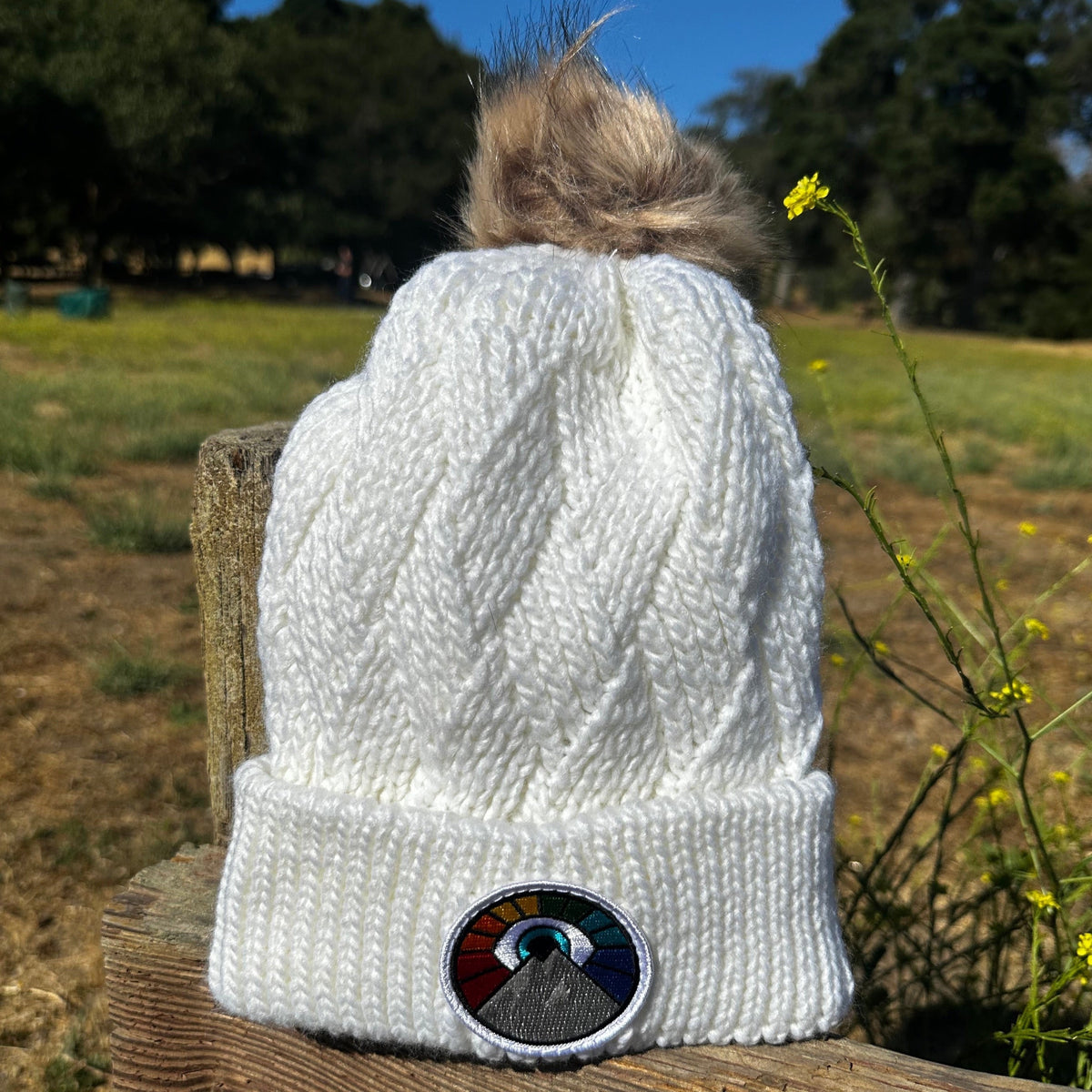 White Kooh Culture faux fur pom beanie with the Evil Eye Sun patch in Rainbow Edition colours
