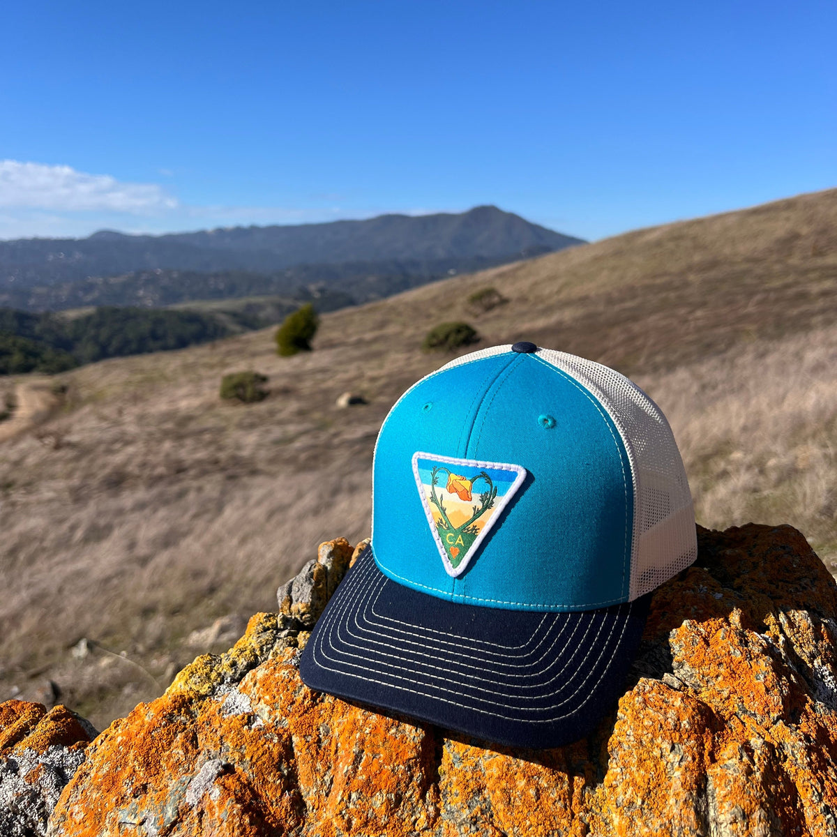 Blue teal and birch and navy Kooh Culture trucker hat with the Poppy CA Love patch