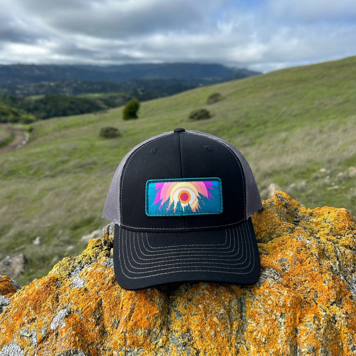 Black and charcoal Kooh Culture trucker hat with the In the Trees patch
