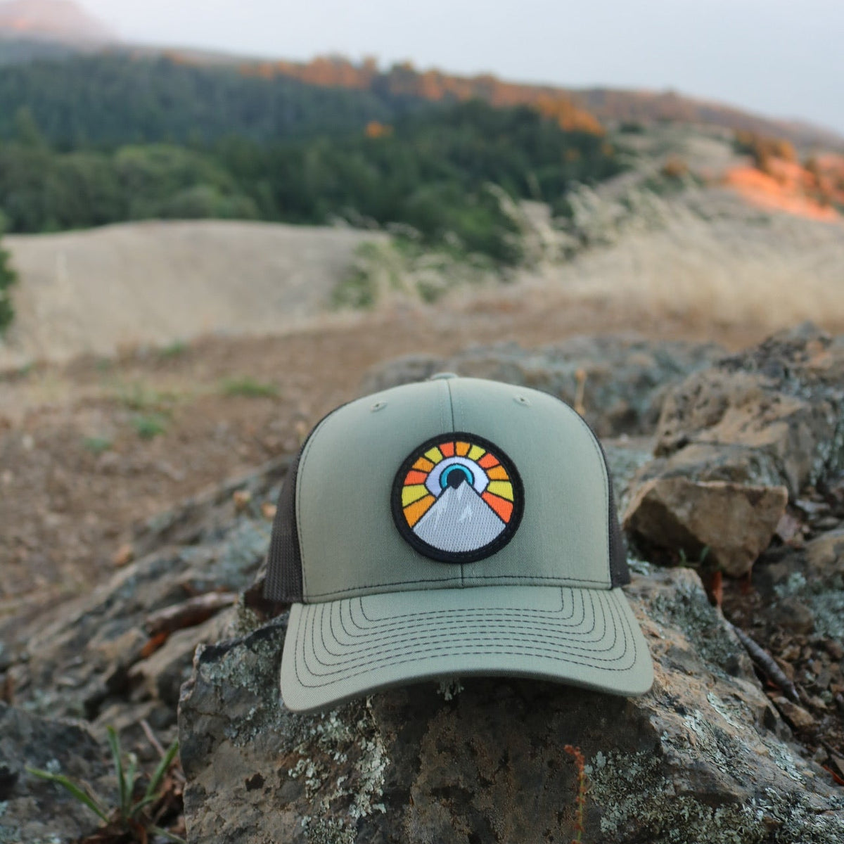 Army green and black Kooh Culture trucker hat with the Evil Eye Sun patch