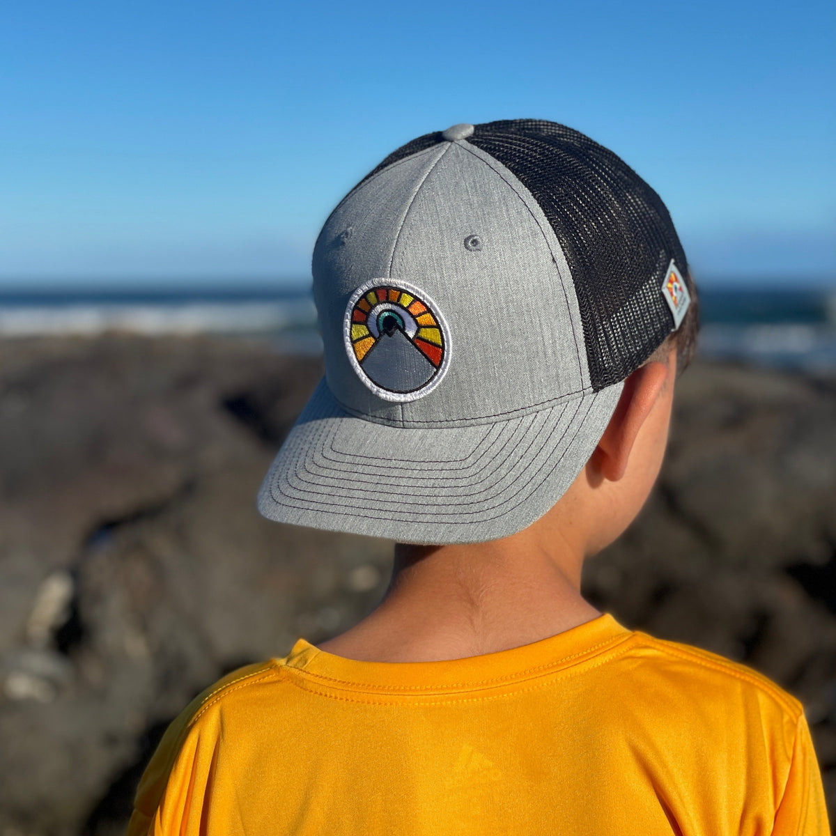 Grey and black Kooh Culture youth trucker hat with the Evil Eye Sun patch