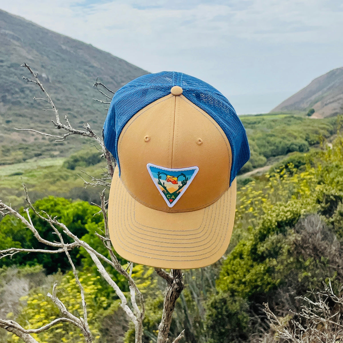 Biscuit and true blue Kooh Culture trucker hat with the Poppy CA Love patch