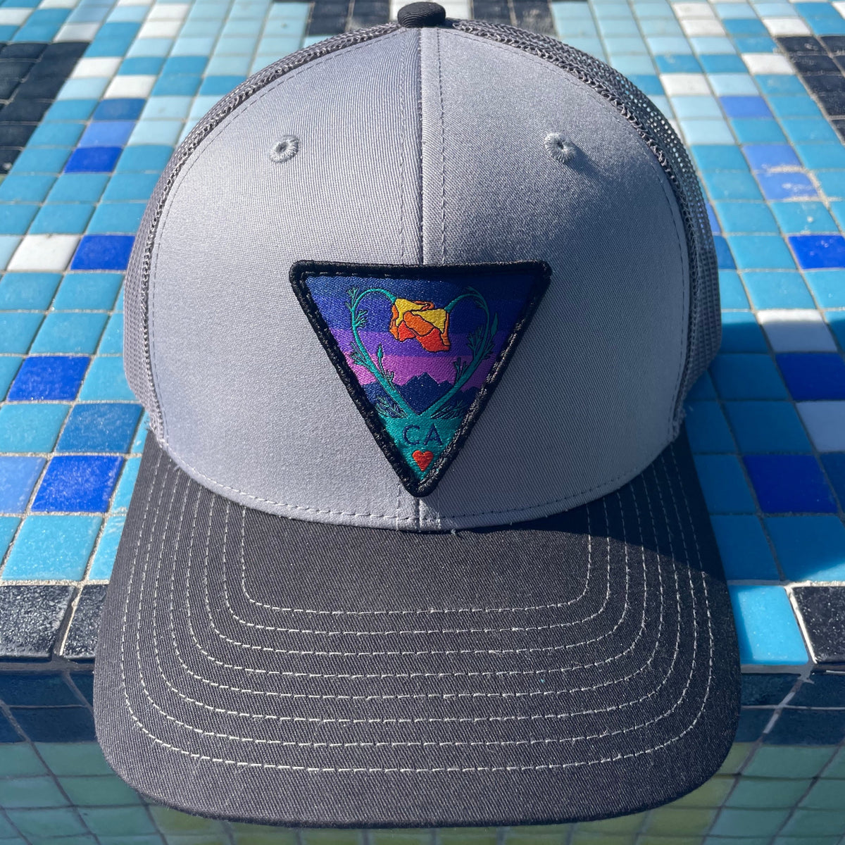 Grey and charcoal and black Kooh Culture trucker hat with the Poppy CA Love patch in Night Mode colours