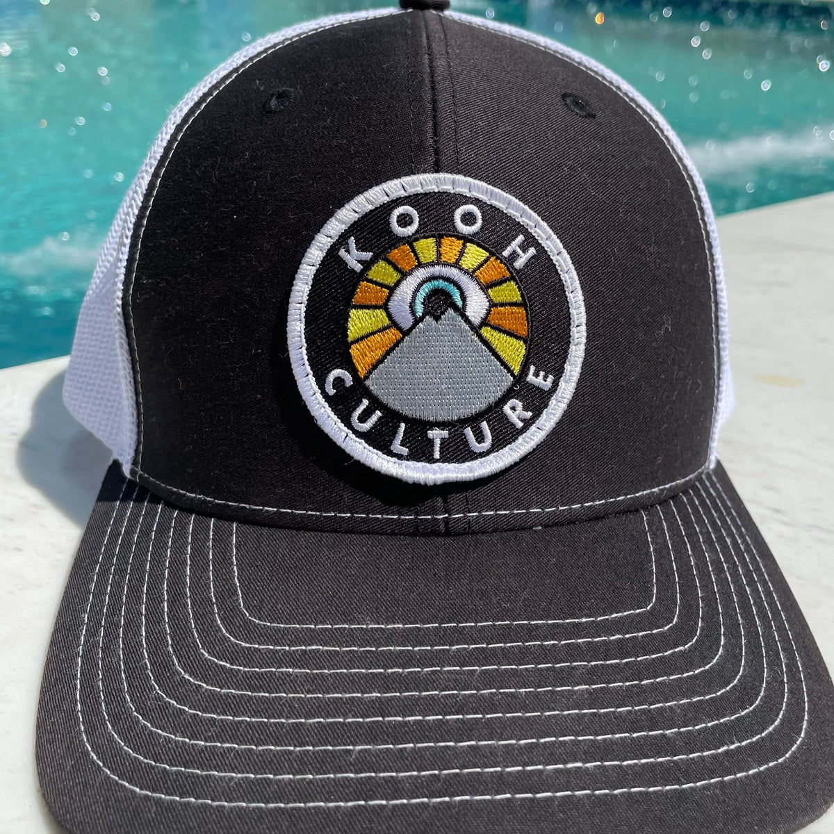 Black and white Kooh Culture trucker hat with the mountain and sun badge