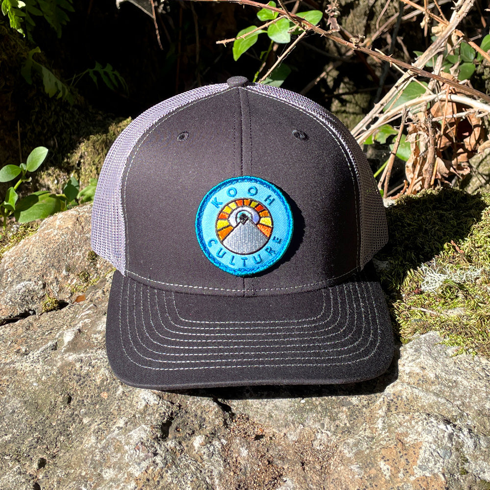 Black and charcoal Kooh Culture trucker hat with the mountain and sun badge